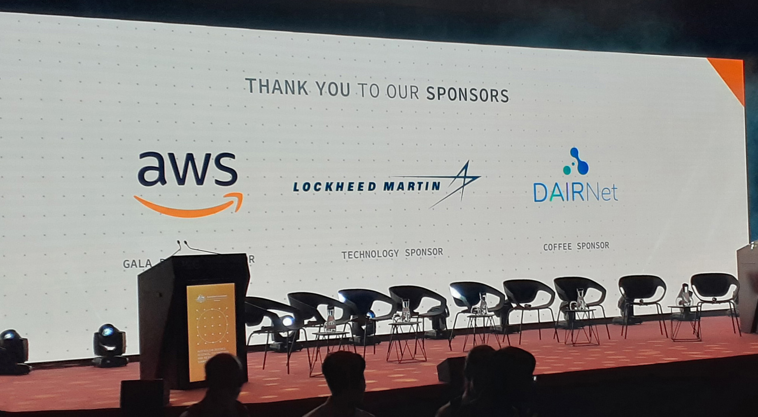 Stage at the ADSTAR Summit with a backdrop that says "Thank you to our sponsors" followed by the logos of AWS as gala dinner sponsor, Lockheed Martin as technology sponsor and DAIRNet as coffee sponsor.